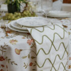 Emerson Olive linen drape featuring a modern wave pattern in olive green, elegantly styled on a table setting with floral tablecloth, plates, and glassware.
