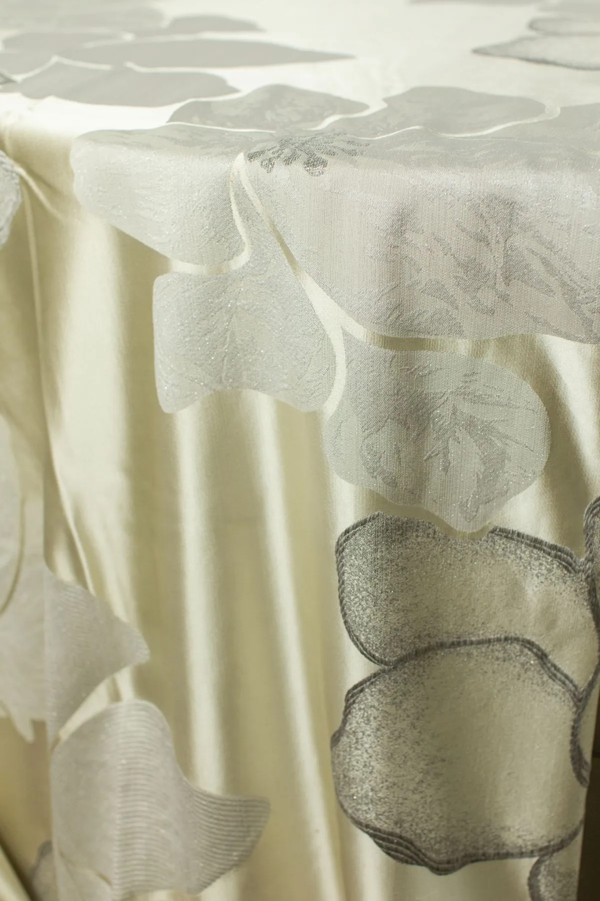 Ivory satin table linen with oversized floral appliqué detailing along the edge.