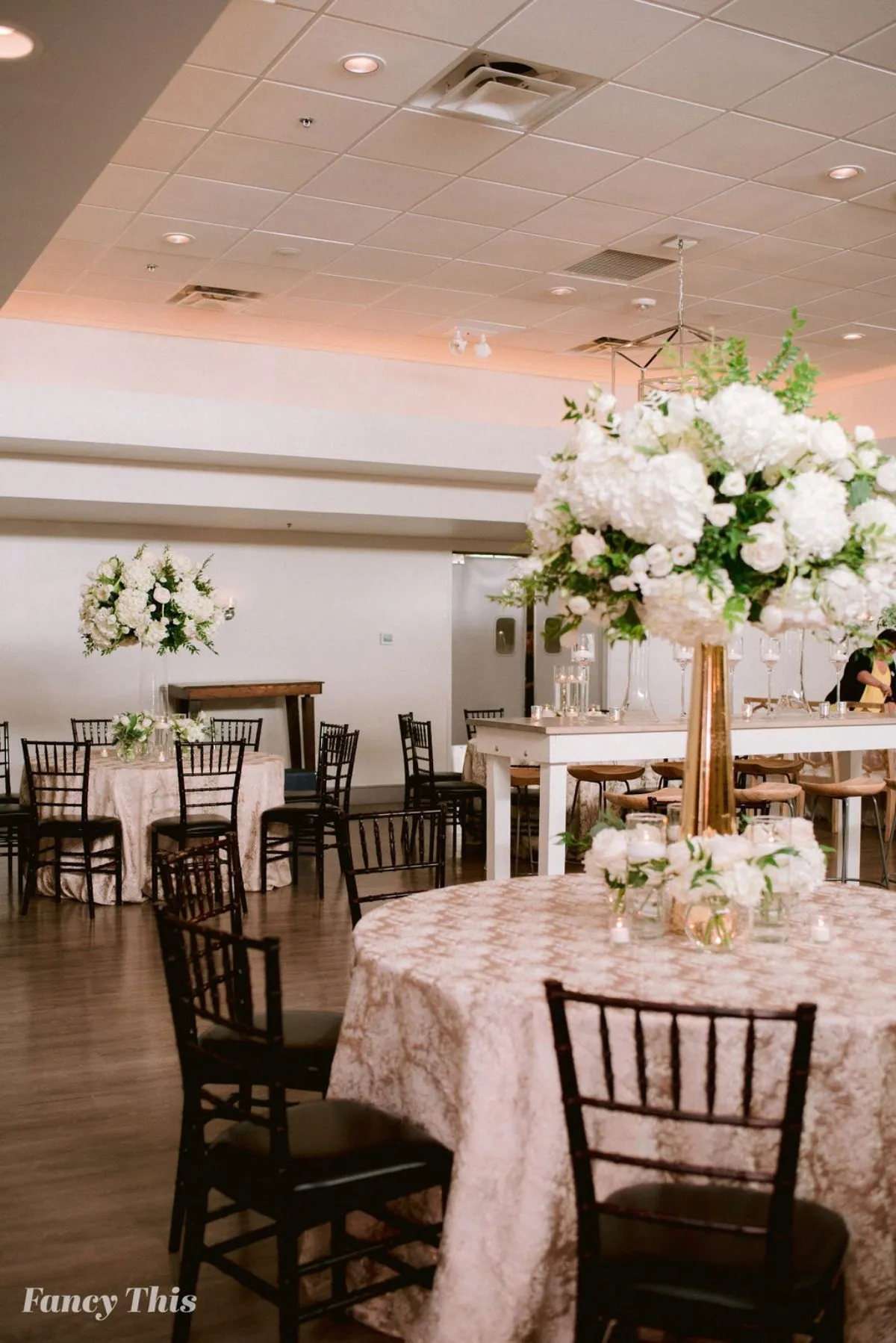 Reception space featuring blush custom table linens and tall white floral centerpieces.