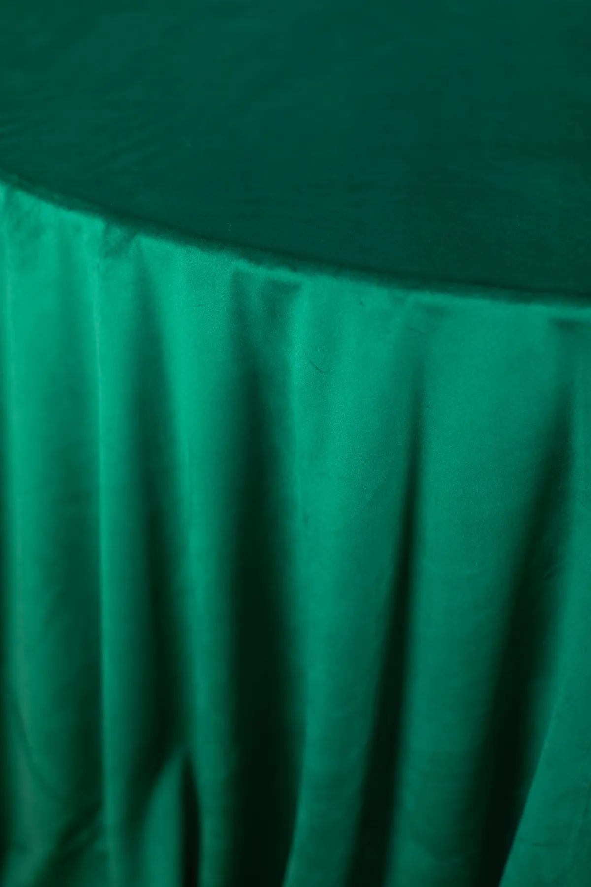 Close-up of emerald green luxury linen tablecloth with elegant gathered drape.