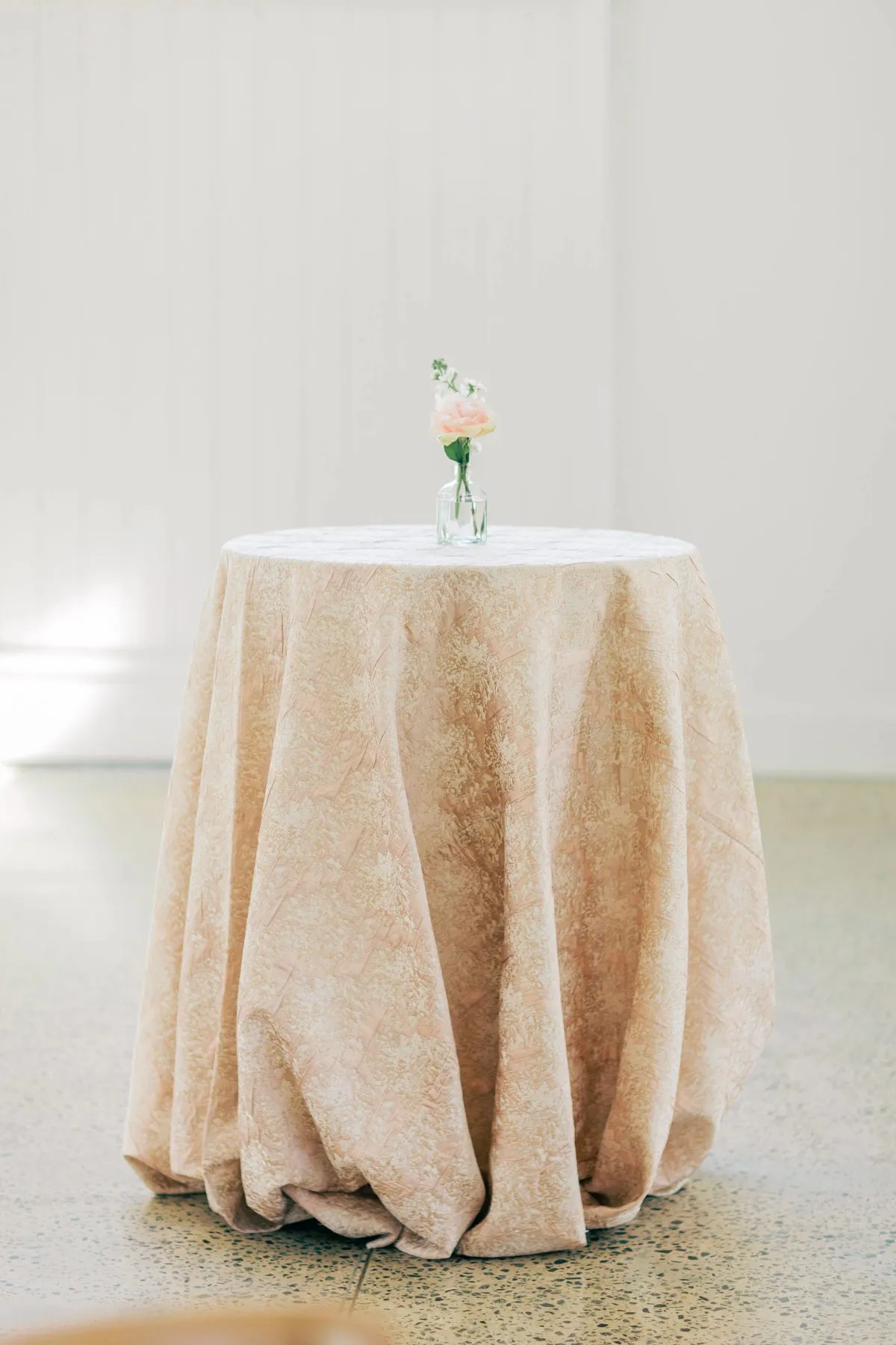 Round cocktail table draped in blush custom linen with a single bud vase centerpiece.