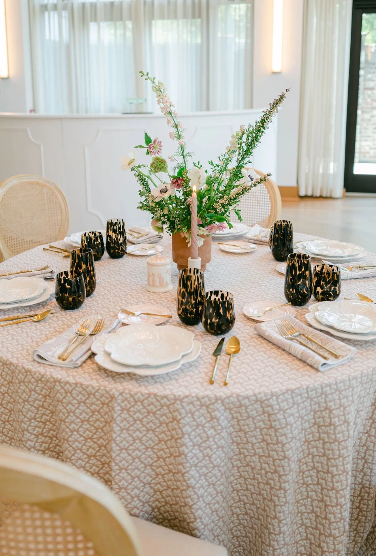 Round reception table styled with patterned luxury linen, gold flatware, and dark glassware.