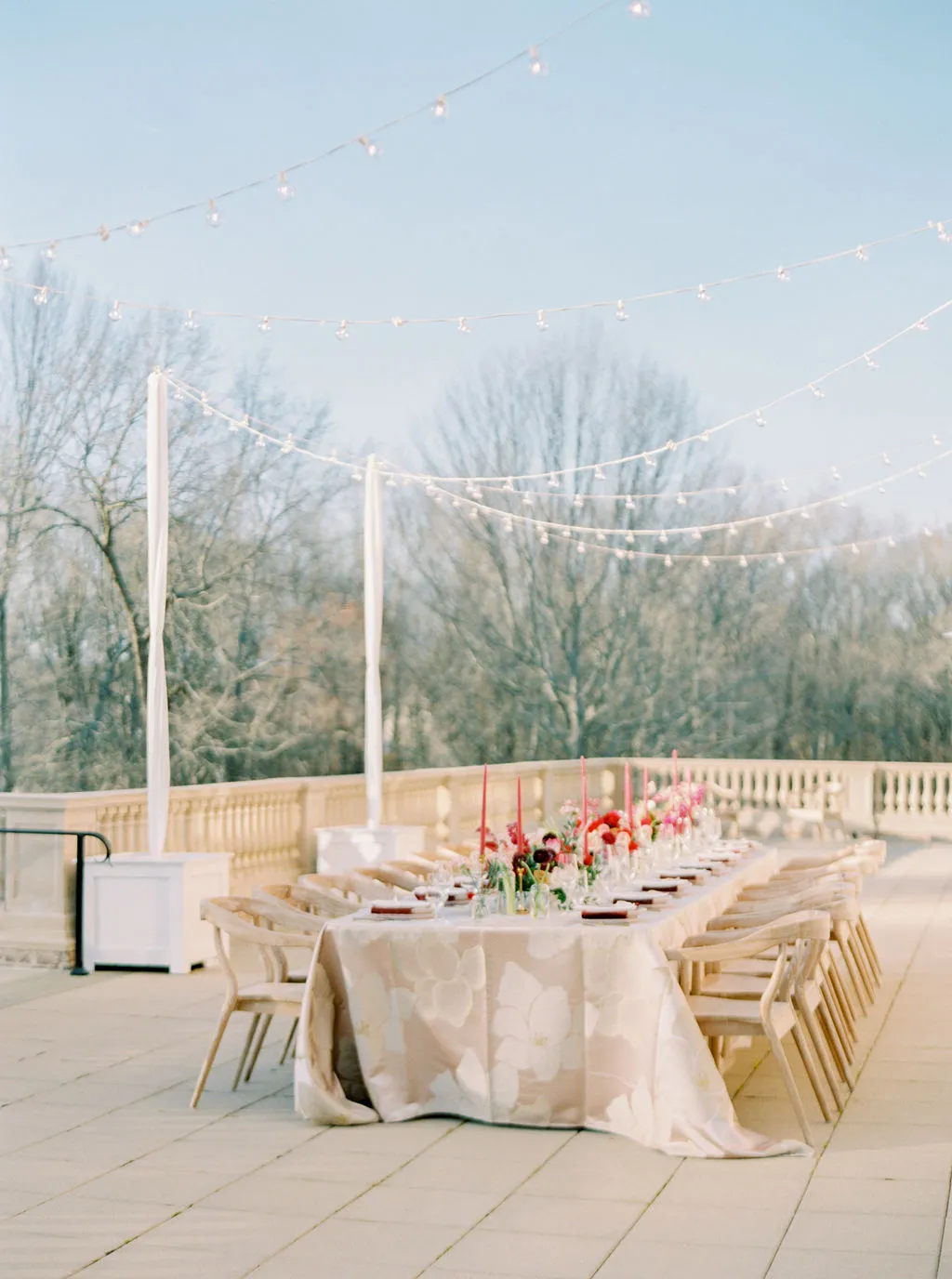 Outdoor reception table with floral luxury tablecloth and string lights.