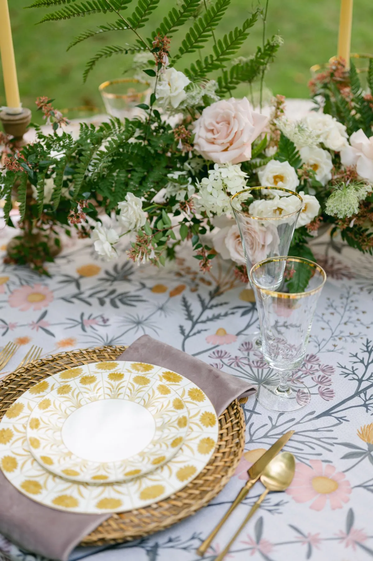 Botanical tablecloth with gold-rimmed plates and floral centerpiece.