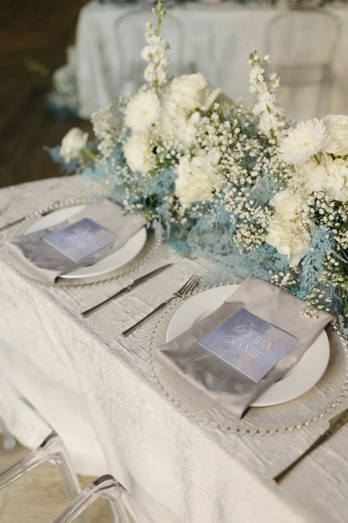 Ivory head table featuring textured custom linen and abundant white floral arrangements.