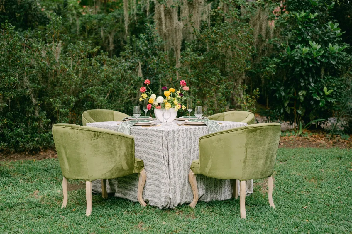 Outdoor dining table with textured striped linen and green velvet chairs.