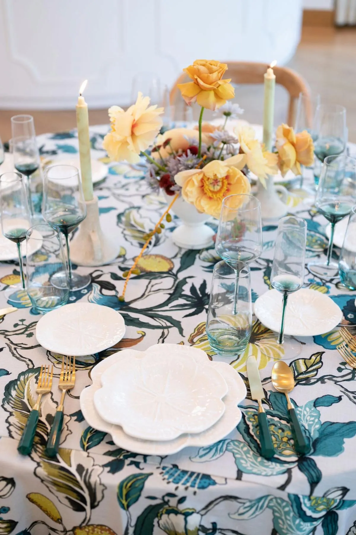 Bold botanical tablecloth styled with yellow florals, teal glassware, and gold accents.