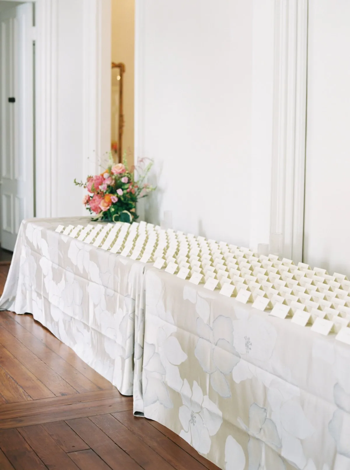 Escort card table draped in floor-length ivory floral linen for a seamless, polished look.