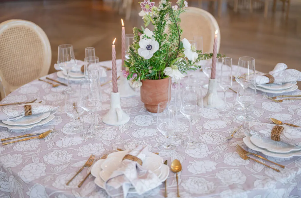 Round table with blush floral linen, candles, and soft neutral place settings - Curated Linen Collection Round table with blush floral linen, candles, and soft neutral place settings