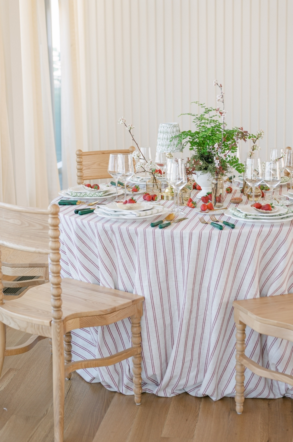 Striped custom table linen styled with layered plates, fresh strawberries, greenery centerpieces, and light wood chairs for a modern event setting. - Curated Linen Collection Striped custom table linen styled with layered plates, fresh strawberries, greenery centerpieces, and light wood chairs for a modern event setting.