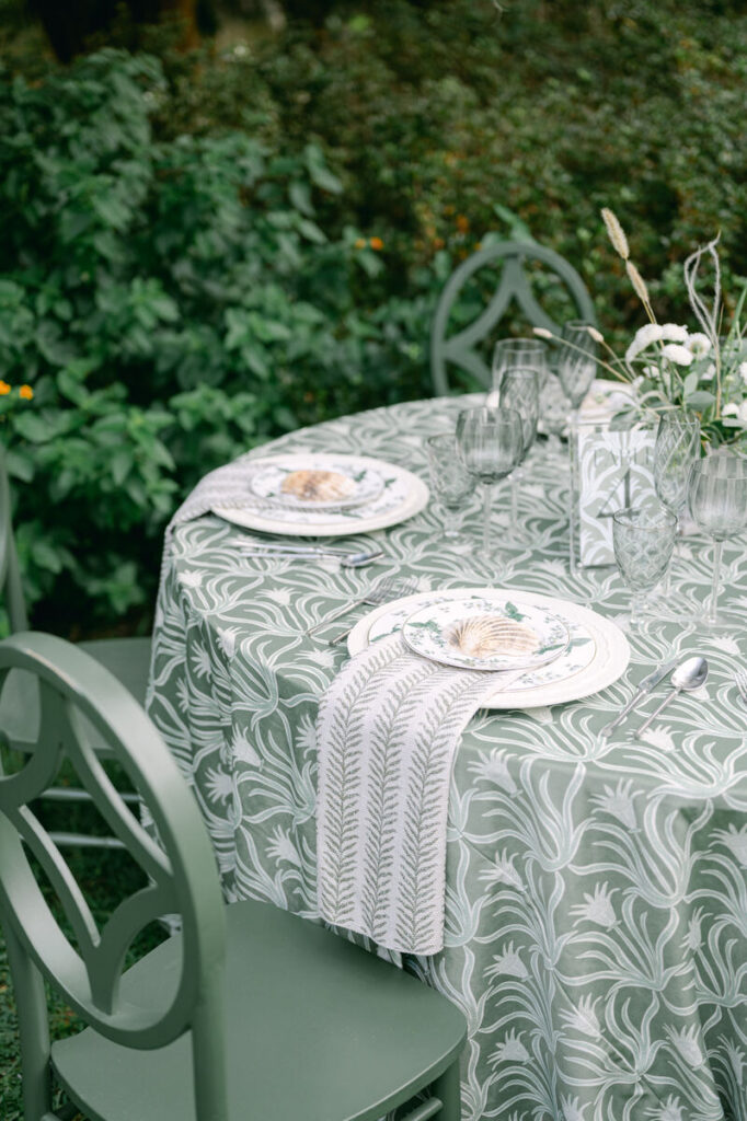 Green botanical linen with patterned plates and folded napkins for an outdoor summer wedding table. - Curated Linen Collection Elegant wedding tablescape with patterned linens and textured napkins.