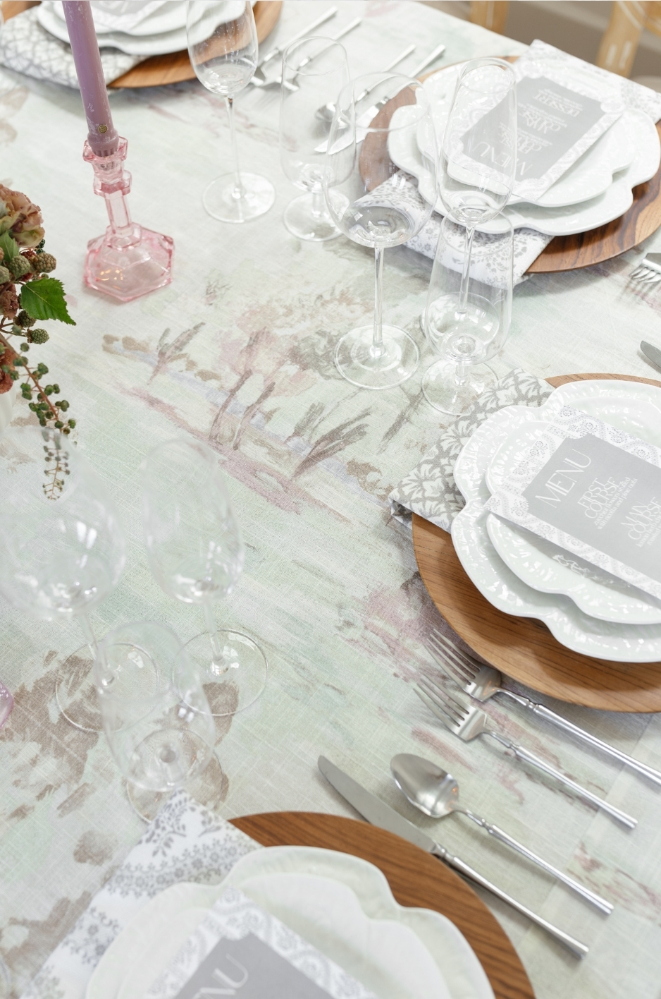 Close-up of pastel printed event linen with layered place settings, wood chargers, glassware, and pink candleholder. - Curated Linen Collection Close-up of pastel printed event linen with layered place settings, wood chargers, glassware, and pink candleholder.