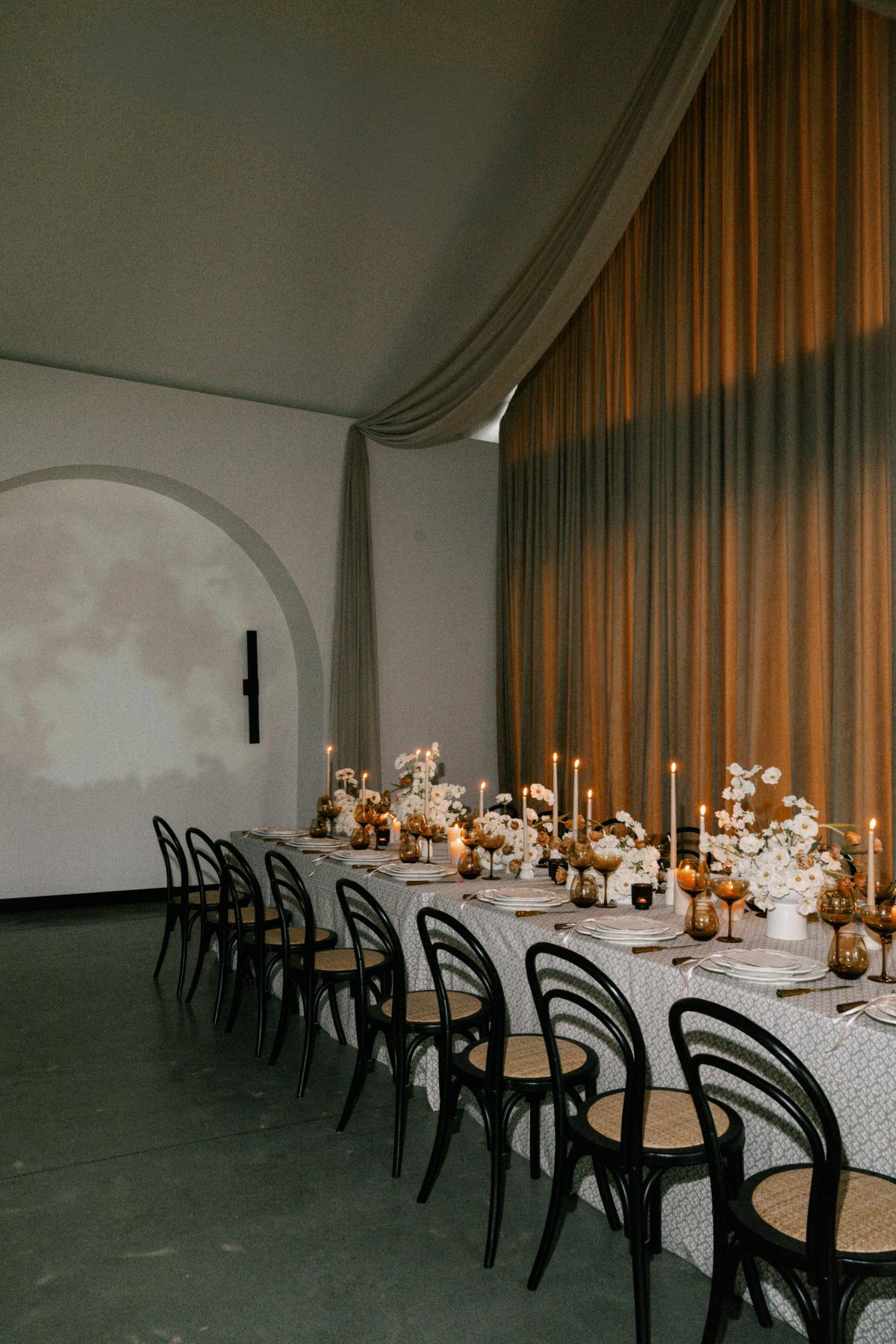 Moody summer wedding reception table with patterned linen, candlelight, florals, black chairs, and soft draping. - Curated Linen Collection Elegant tablescape with linen tablecloths and drapery illustrating pattern scale and linen selection for weddings.