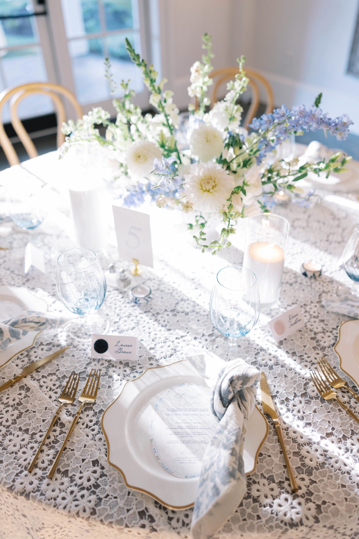 Bright wedding table with white and blue florals, lace linen, candles, blue glassware, and place cards. - Curated Linen Collection Bright wedding table with white and blue florals, lace linen, candles, blue glassware, and place cards.