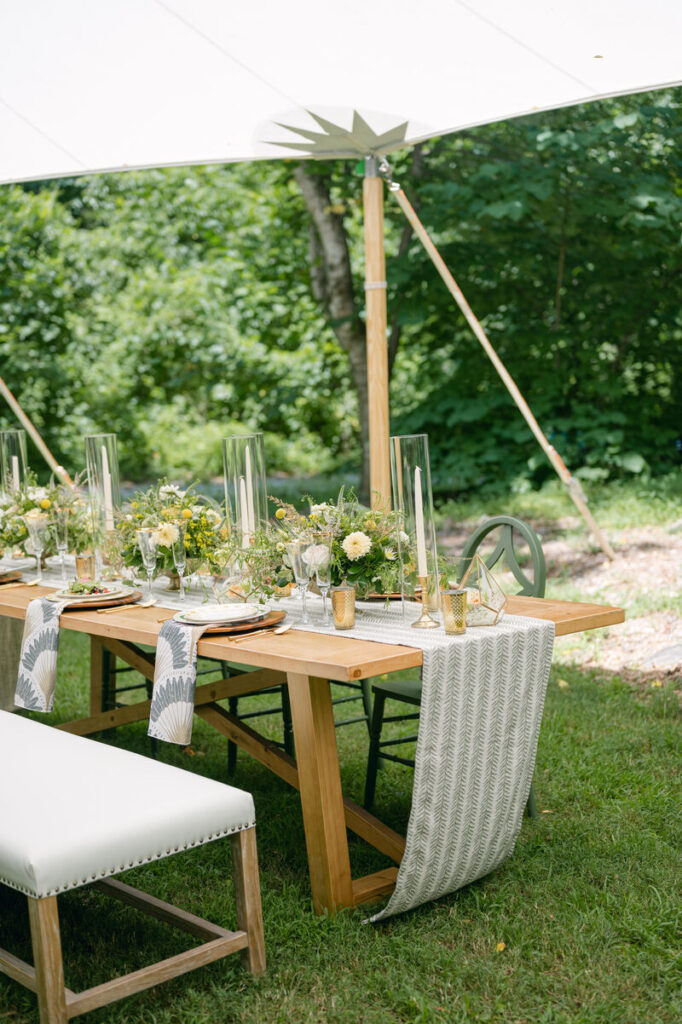 Outdoor tented event table with wood dining table, linen runners, glassware, and summer floral centerpieces. - Curated Linen Collection Outdoor tented event table with wood dining table, linen runners, glassware, and summer floral centerpieces.