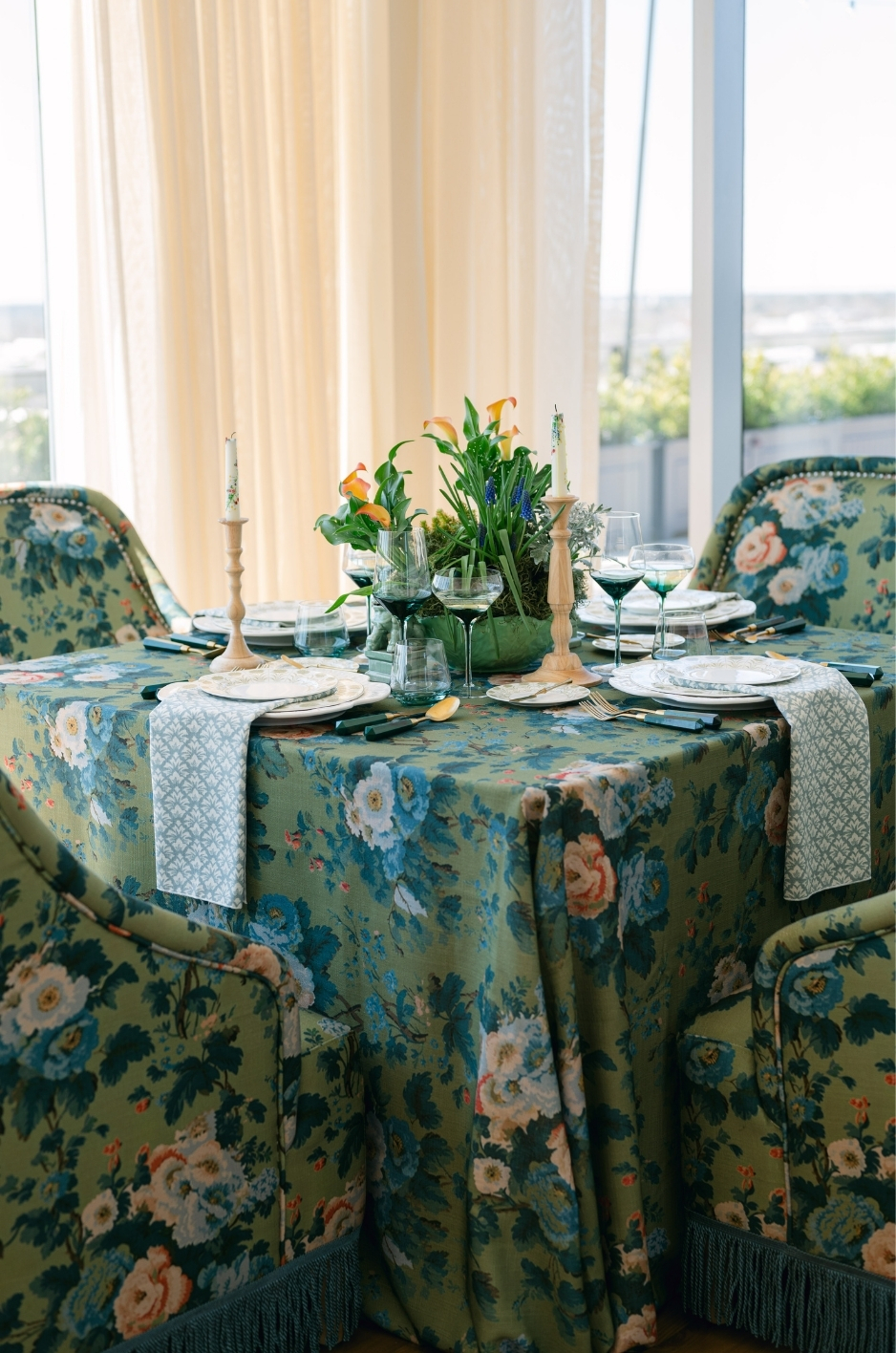 Bright indoor dining table with blue floral linen, matching upholstered chairs, candles, and floral centerpiece. - Curated Linen Collection Bright indoor dining table with blue floral linen, matching upholstered chairs, candles, and floral centerpiece.