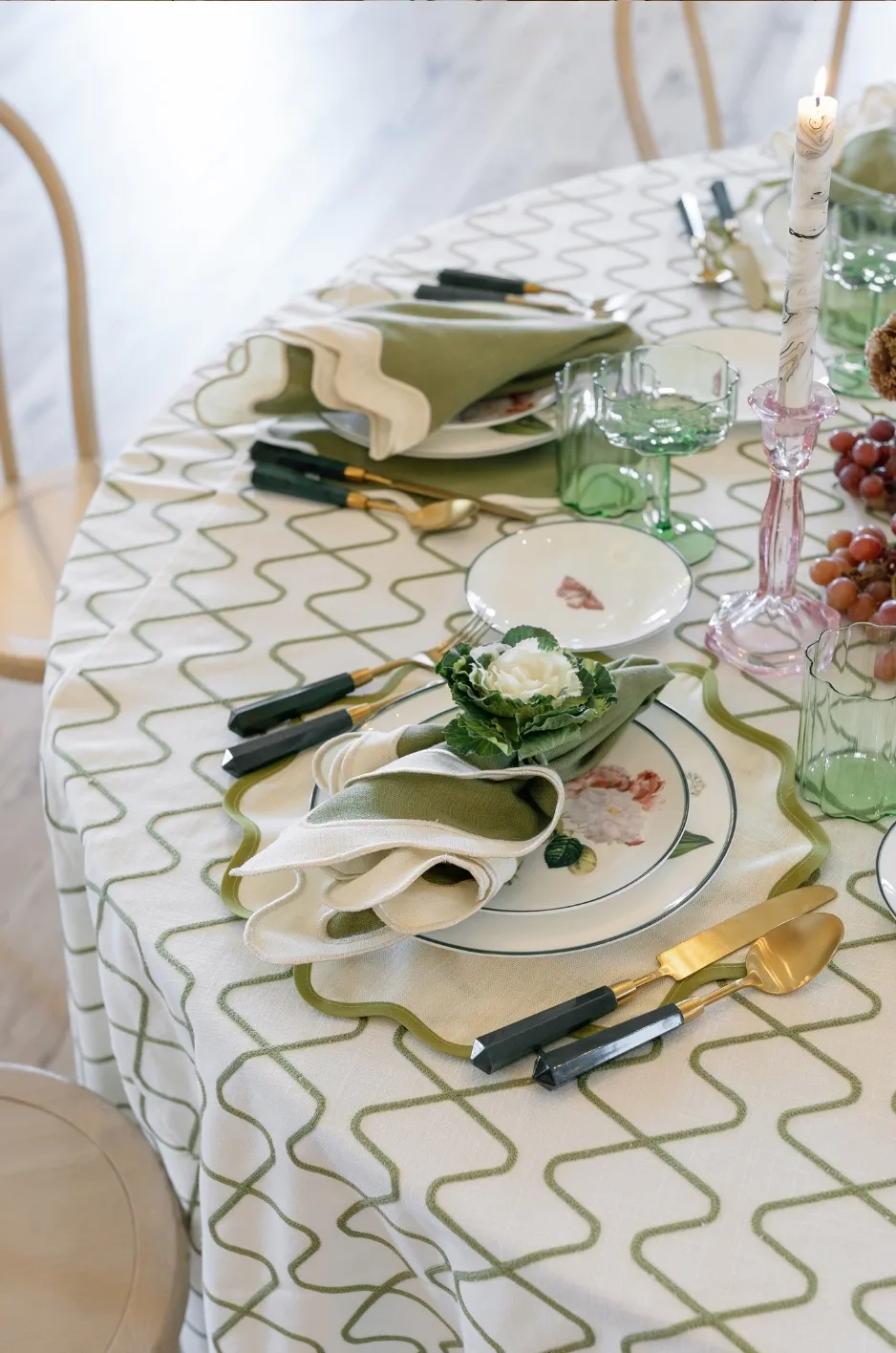 Round reception table with green patterned linen, folded napkins, colored glassware, and gold flatware for a refined wedding design - Curated Linen Collection Round reception table with green patterned linen, folded napkins, colored glassware, and gold flatware for a refined wedding design