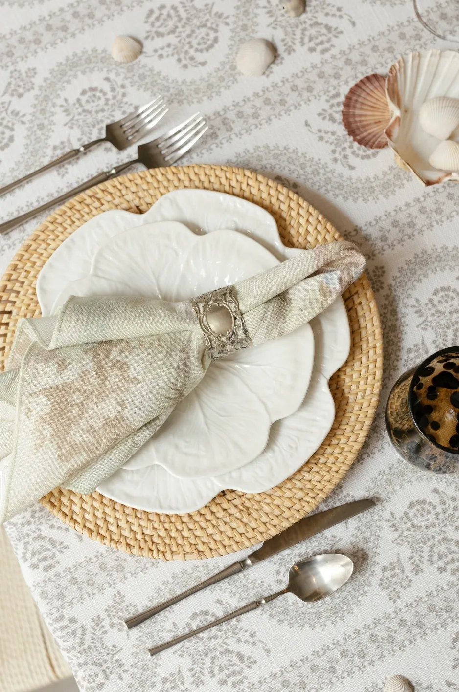 Luxury place setting with patterned linen, woven charger, floral plate, napkin ring, and neutral cloth napkin - Curated Linen Collection Luxury place setting with patterned linen, woven charger, floral plate, napkin ring, and neutral cloth napkin