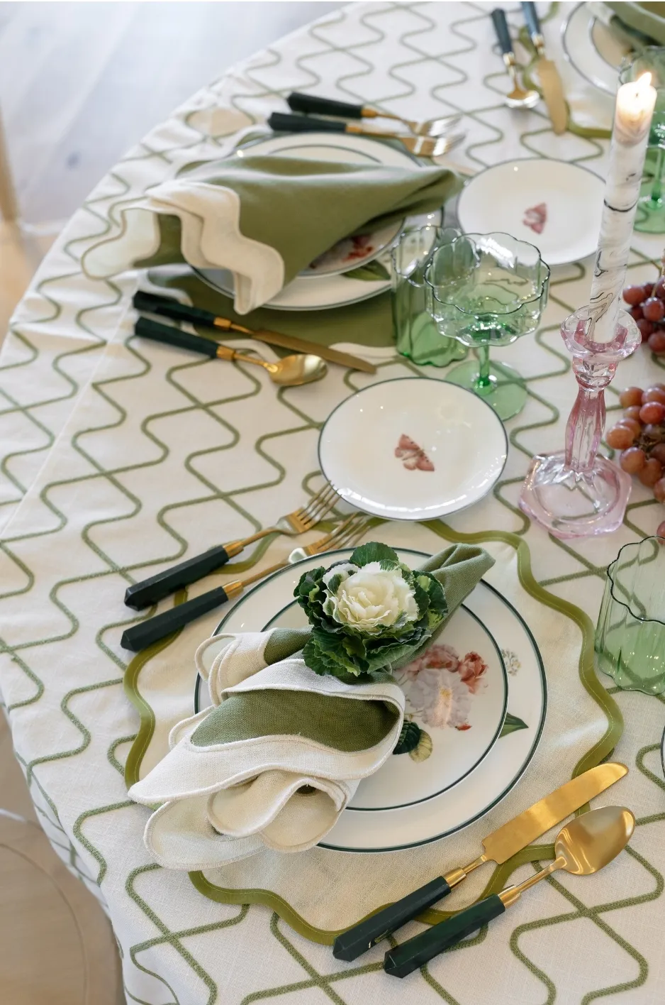 Patterned green designer linen with layered place settings, folded napkins, colored glassware, and gold flatware - Curated Linen Collection Patterned green designer linen with layered place settings, folded napkins, colored glassware, and gold flatware