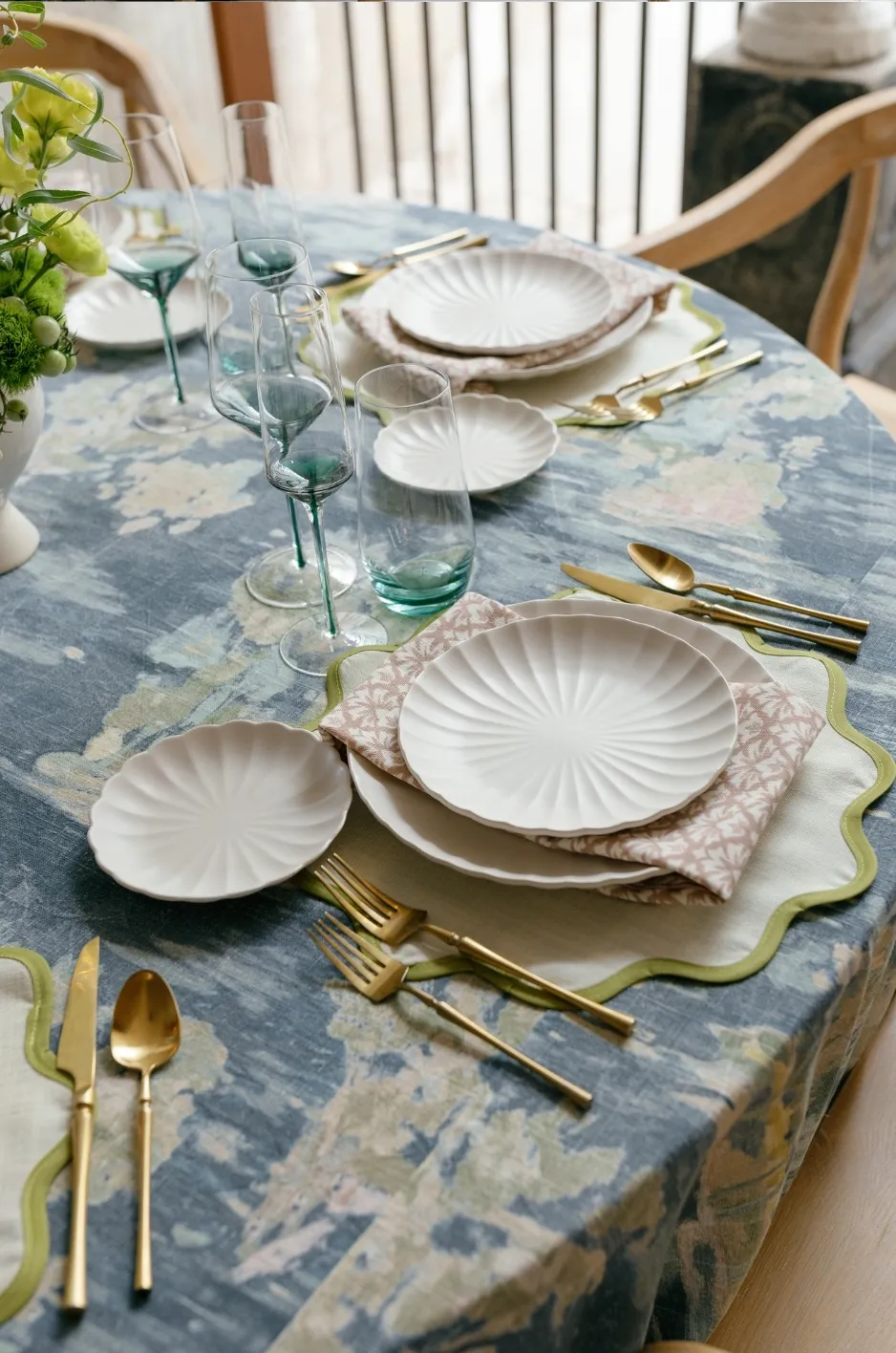 Blue-gray tablecloth with white china and gold flatware - Curated Linen Collection Elegant tablescape with patterned navy linen tablecloth, gold flatware, and ivory plates.