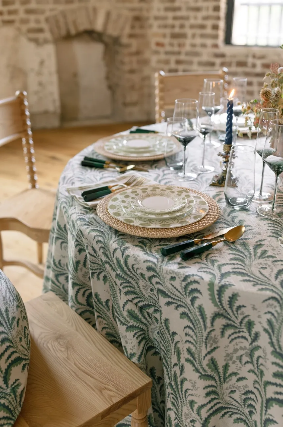 Close-up of a wedding table with green patterned linen, layered plates, glassware, and gold flatware - Curated Linen Collection Close-up of a wedding table with green patterned linen, layered plates, glassware, and gold flatware