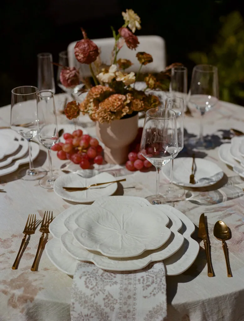 Candlelit celebration table with lace details, white place settings, grapes, florals, and wine glasses - Curated Linen Collection Candlelit celebration table with lace details, white place settings, grapes, florals, and wine glasses