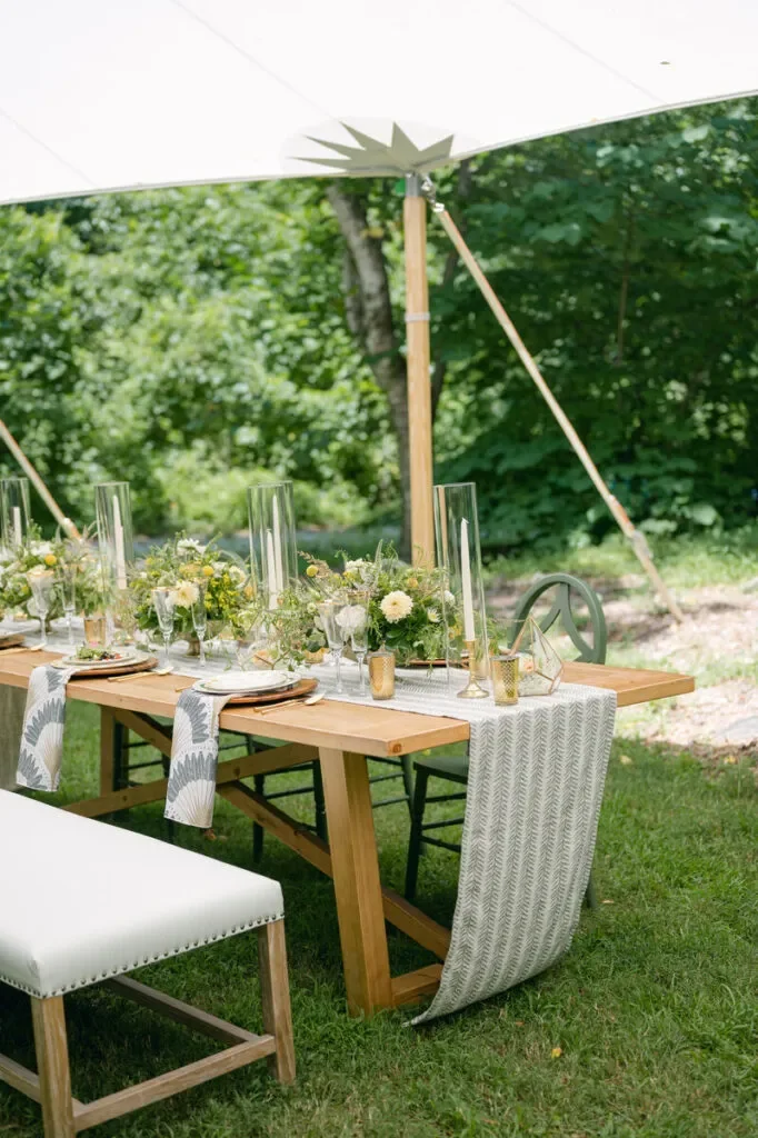 Outdoor wood reception table styled with patterned table runners, garden florals, and tall glass candleholders. Outdoor wood reception table styled with patterned table runners, garden florals, and tall glass candleholders.
