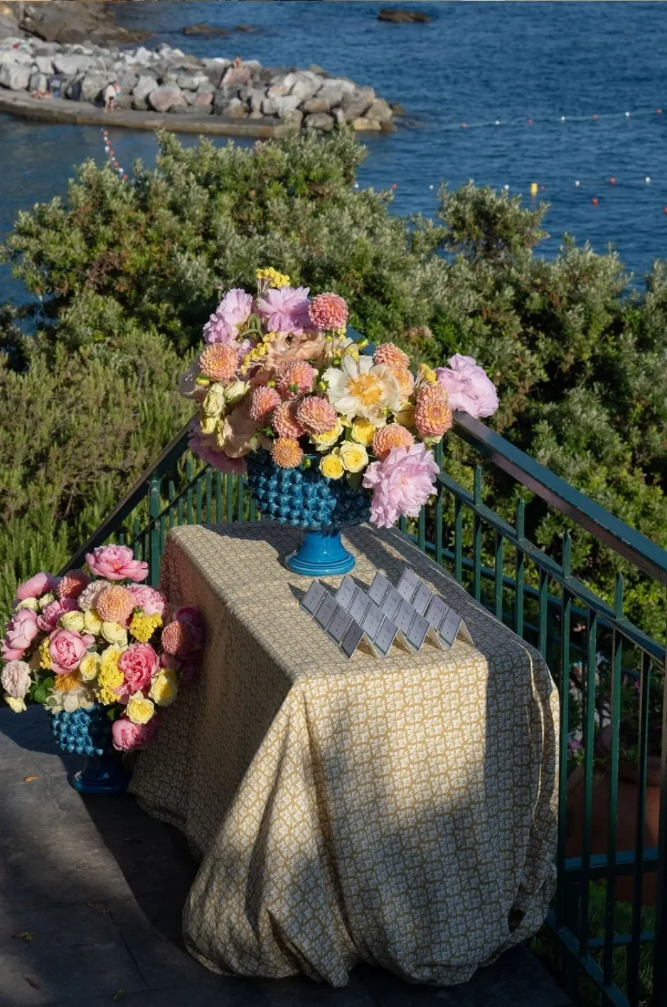 Small event display table with a gold geometric linen, colorful floral arrangements, and arranged place cards. Small event display table with a gold geometric linen, colorful floral arrangements, and arranged place cards.