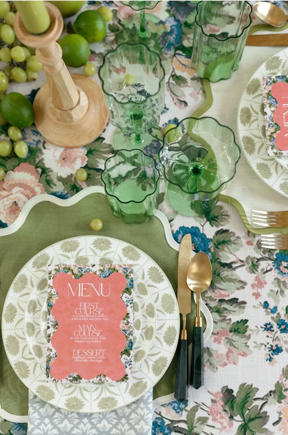 Coral menu card centered over patterned china with green glassware, green-edged linens, gold flatware, and fresh fruit. - Curated Linen Collection Coral menu card centered over patterned china with green glassware, green-edged linens, gold flatware, and fresh fruit.