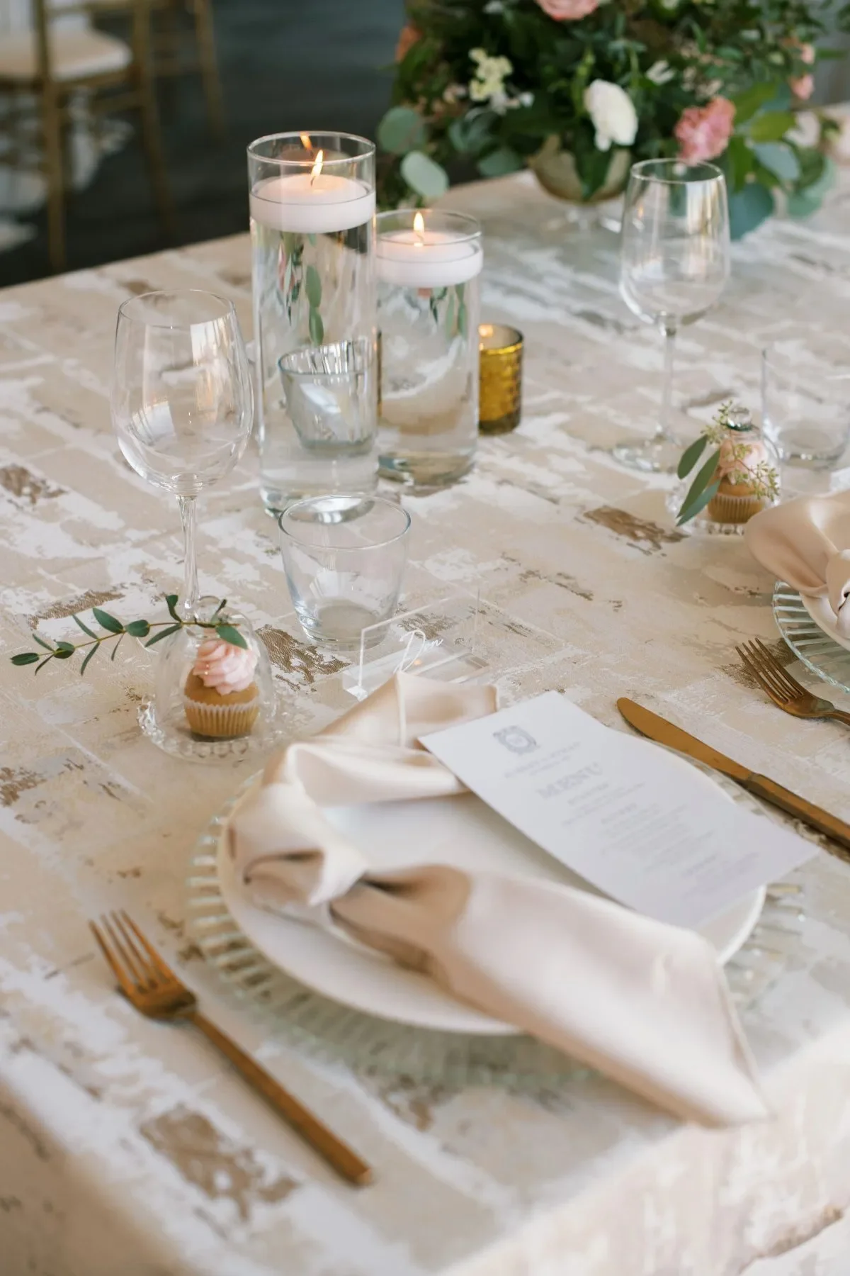 Neutral wedding table styled with a textured linen, blush napkins, glass candleholders, and clear glassware. Neutral wedding table styled with a textured linen, blush napkins, glass candleholders, and clear glassware.