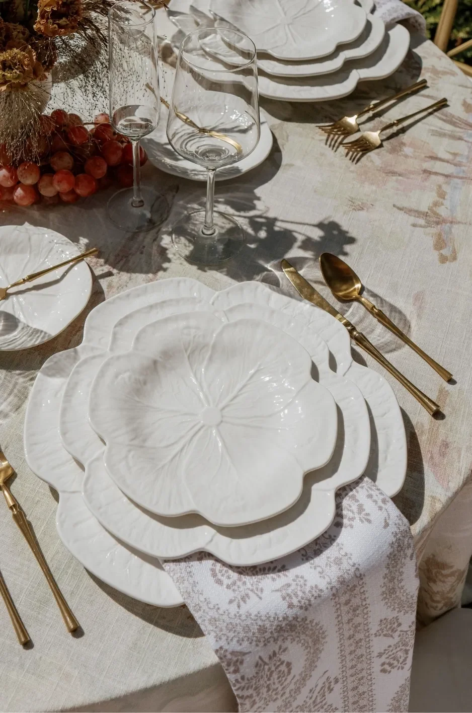 Taupe patterned napkin draped between layered white floral plates on a neutral linen tablecloth. Taupe patterned napkin draped between layered white floral plates on a neutral linen tablecloth.