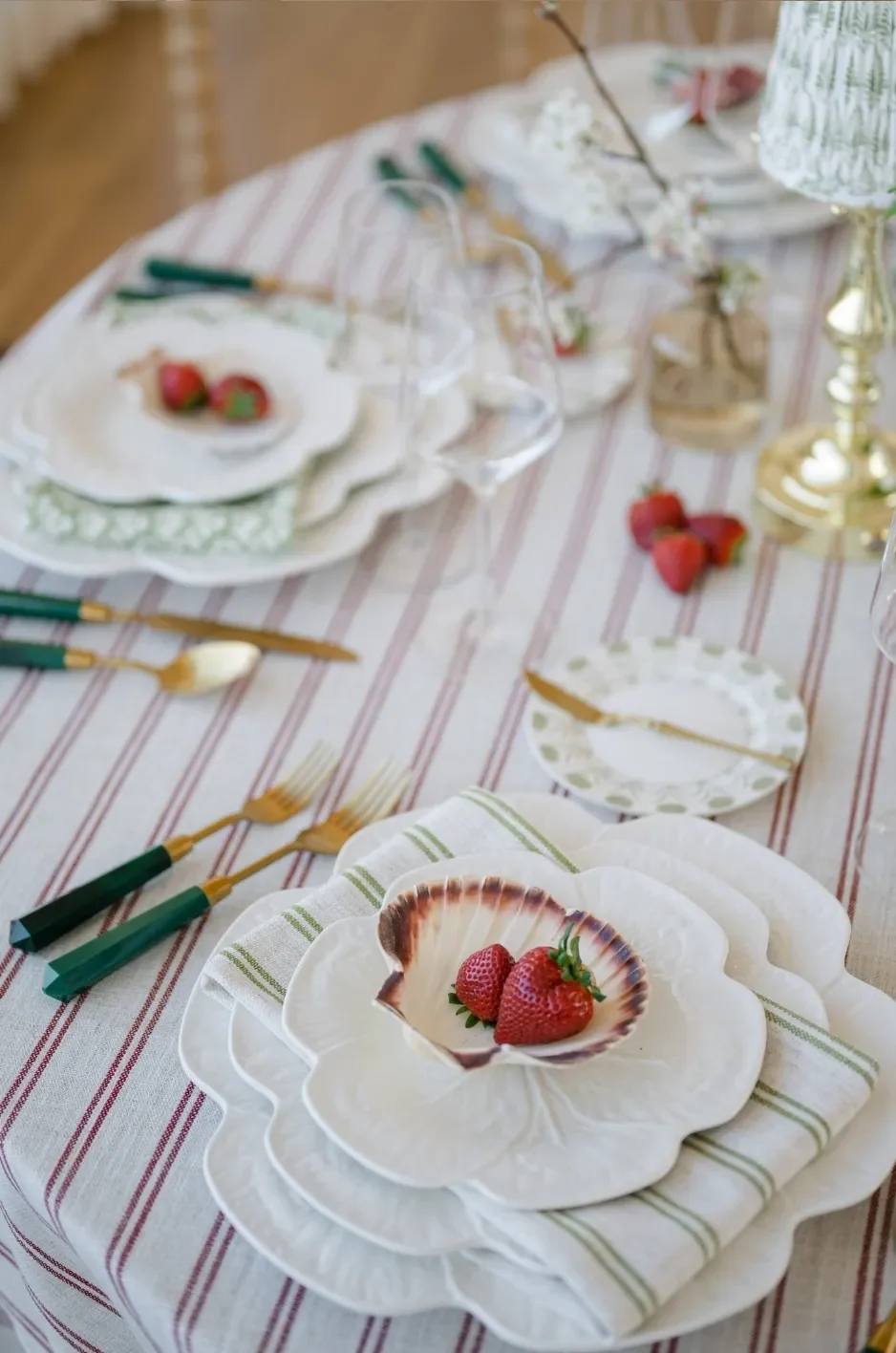 Green striped napkin layered beneath white floral dinnerware on a red striped reception tablecloth. Green striped napkin layered beneath white floral dinnerware on a red striped reception tablecloth.