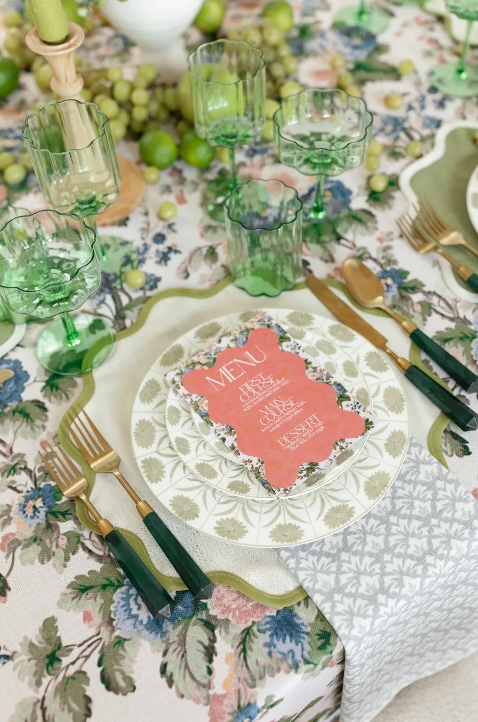 Floral wedding linen with green scalloped glassware, patterned china, coral menu card, green-handled flatware, and fresh fruit. - Curated Linen Collection Floral wedding linen with green scalloped glassware, patterned china, coral menu card, green-handled flatware, and fresh fruit.