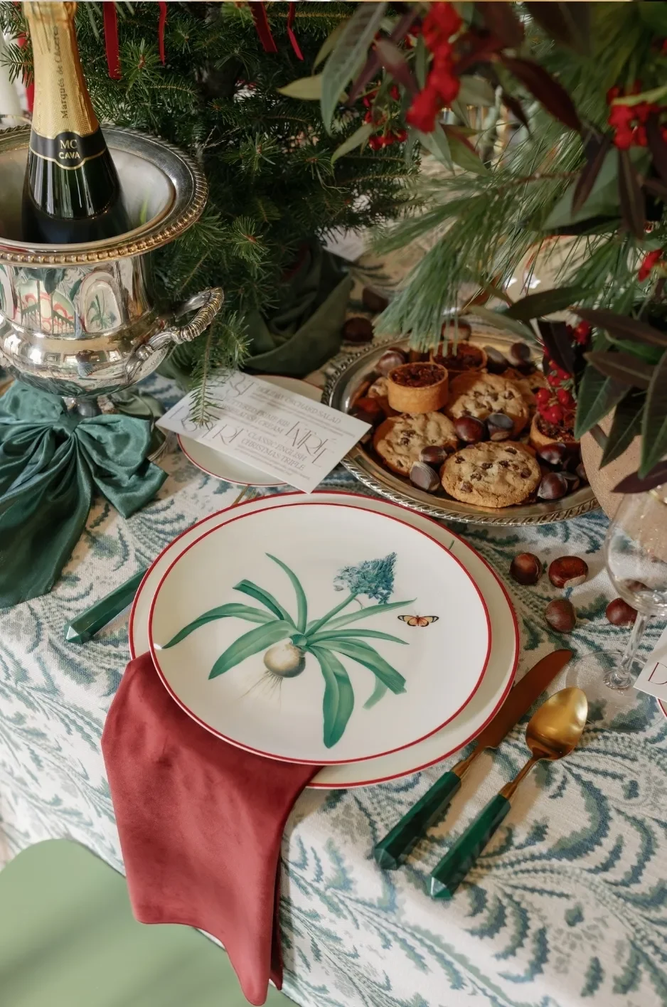 Rust-colored napkin paired with botanical china, green flatware, and a blue-green patterned wedding linen. Rust-colored napkin paired with botanical china, green flatware, and a blue-green patterned wedding linen.