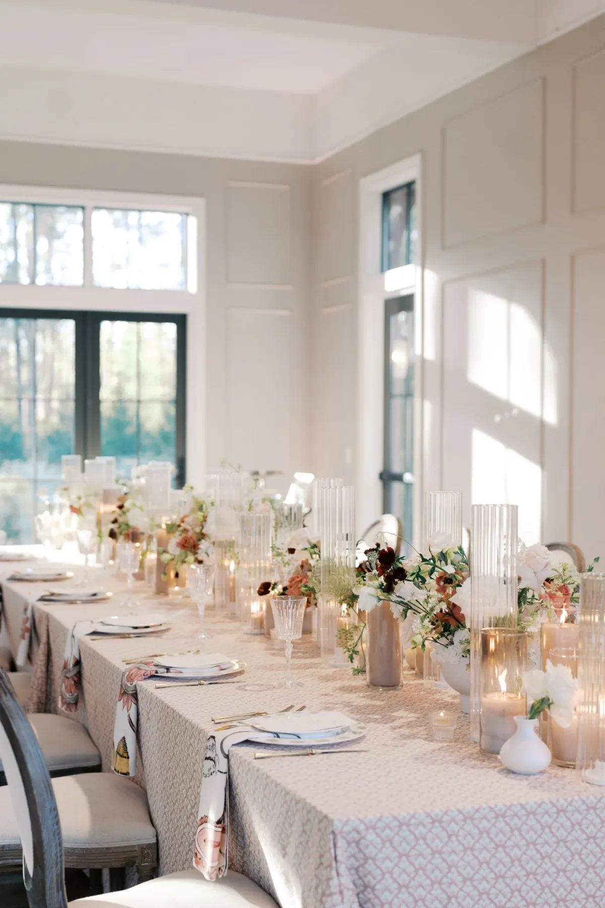 Elegant banquet table styled with a blush geometric linen, glass candleholders, and low floral arrangements. Elegant banquet table styled with a blush geometric linen, glass candleholders, and low floral arrangements.